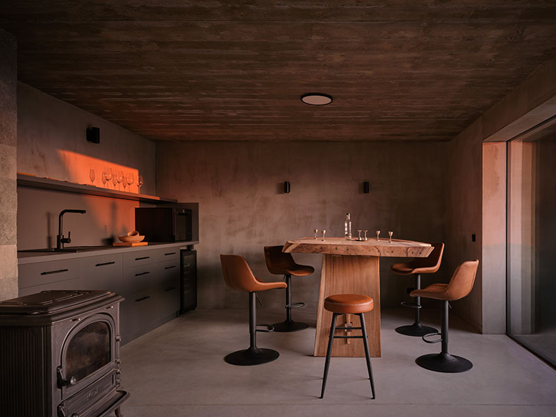 Cocina y zona de bar en el sótano de Senaa con mobiliario oscuro y mesa alta de madera