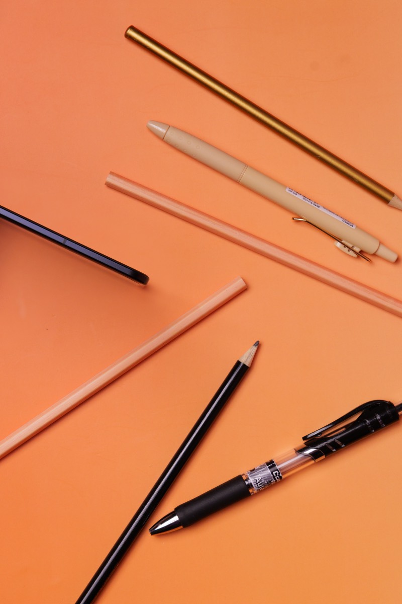 Honor Magic V5: smartphone Honor Magic V5 camuflado entre lapiceros en una foto de estudio sobre un fondo naranja.