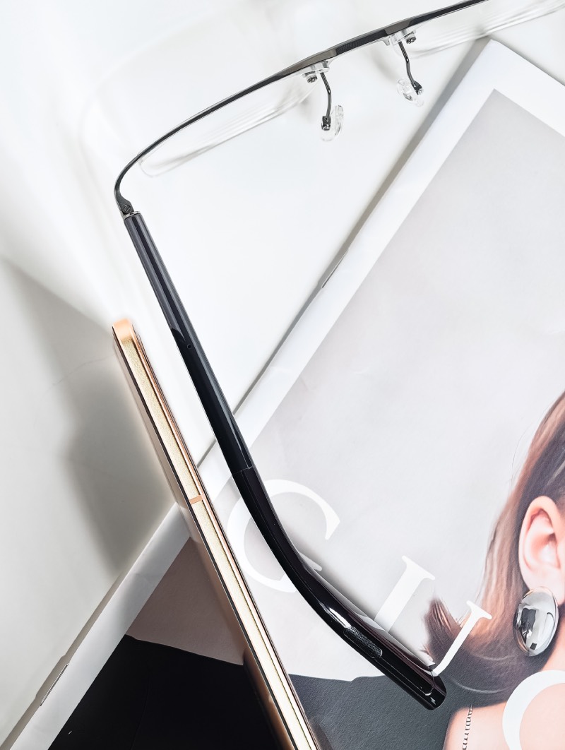 Honor Magic V5: smartphone Honor Magic V5 de perfil sobre una revista de moda y junto a la patilla de unas gafas de ver.