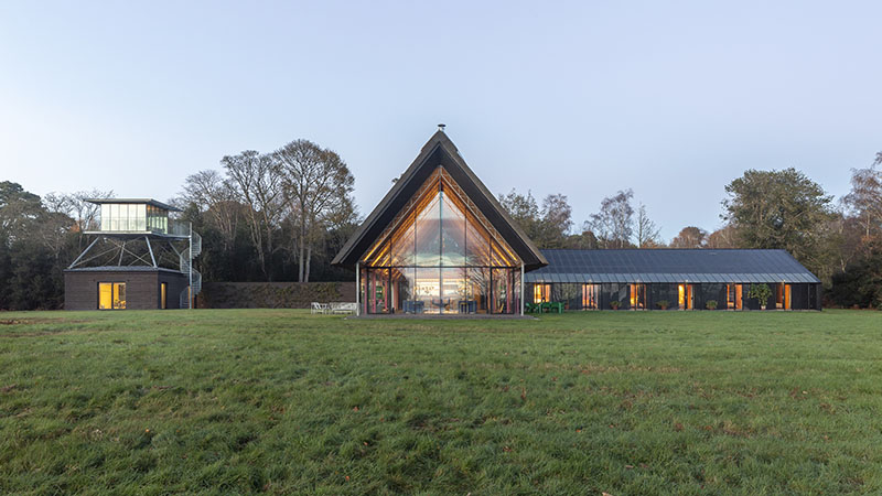Housestead Sanei y Hopkins arquitectos: vista de la casa con forma de invernadero. Rodeada de un prado verde