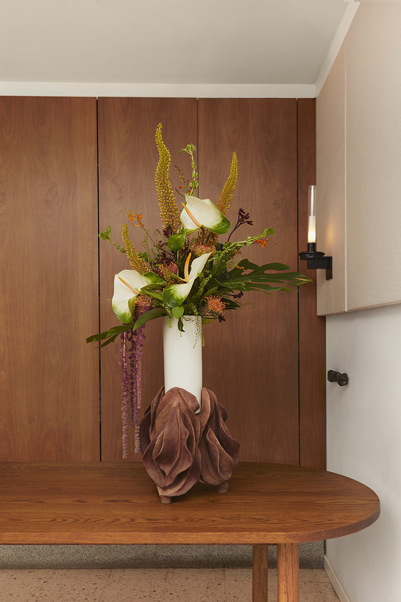 Florero de Ofenhaus con base escultórica y flores blancas sobre una mesa de madera