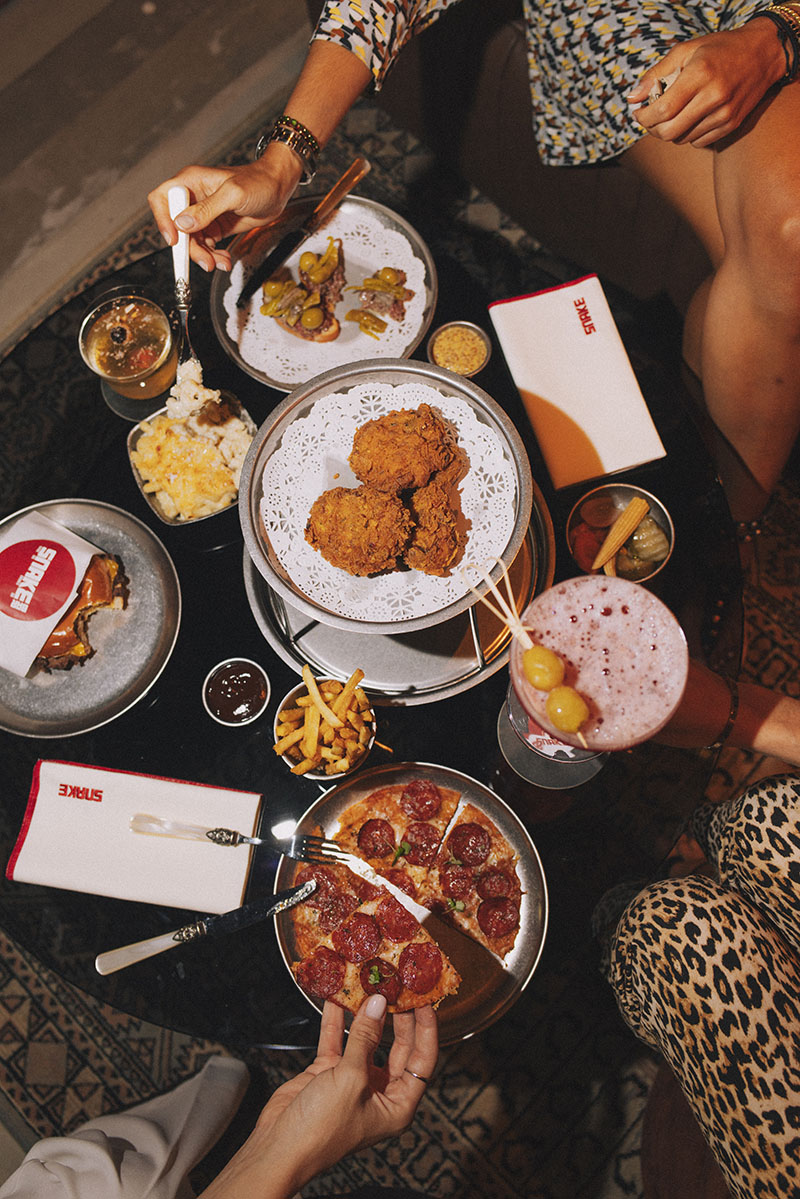 Mesa con pollo frito, pizza, burger y cócteles en Snake Bar Madrid