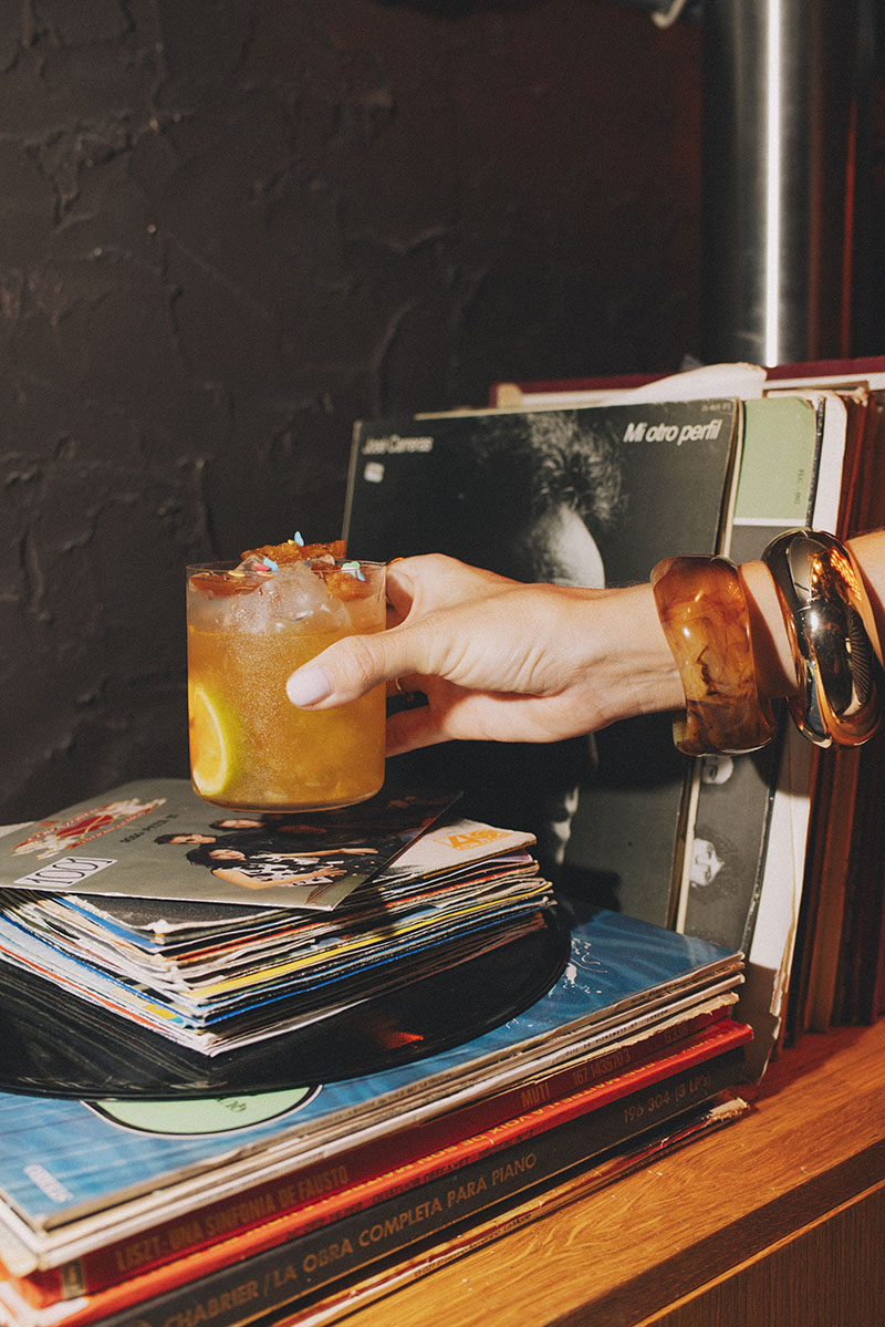 Mano con cóctel sobre vinilos en Snake Bar Madrid