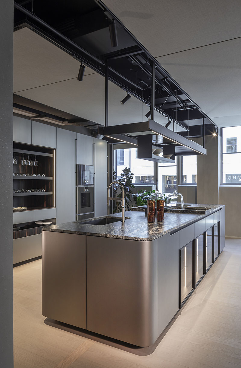 Isla central de la cocina metálica con formas curvas de Arrital, con encimera de piedra veteada