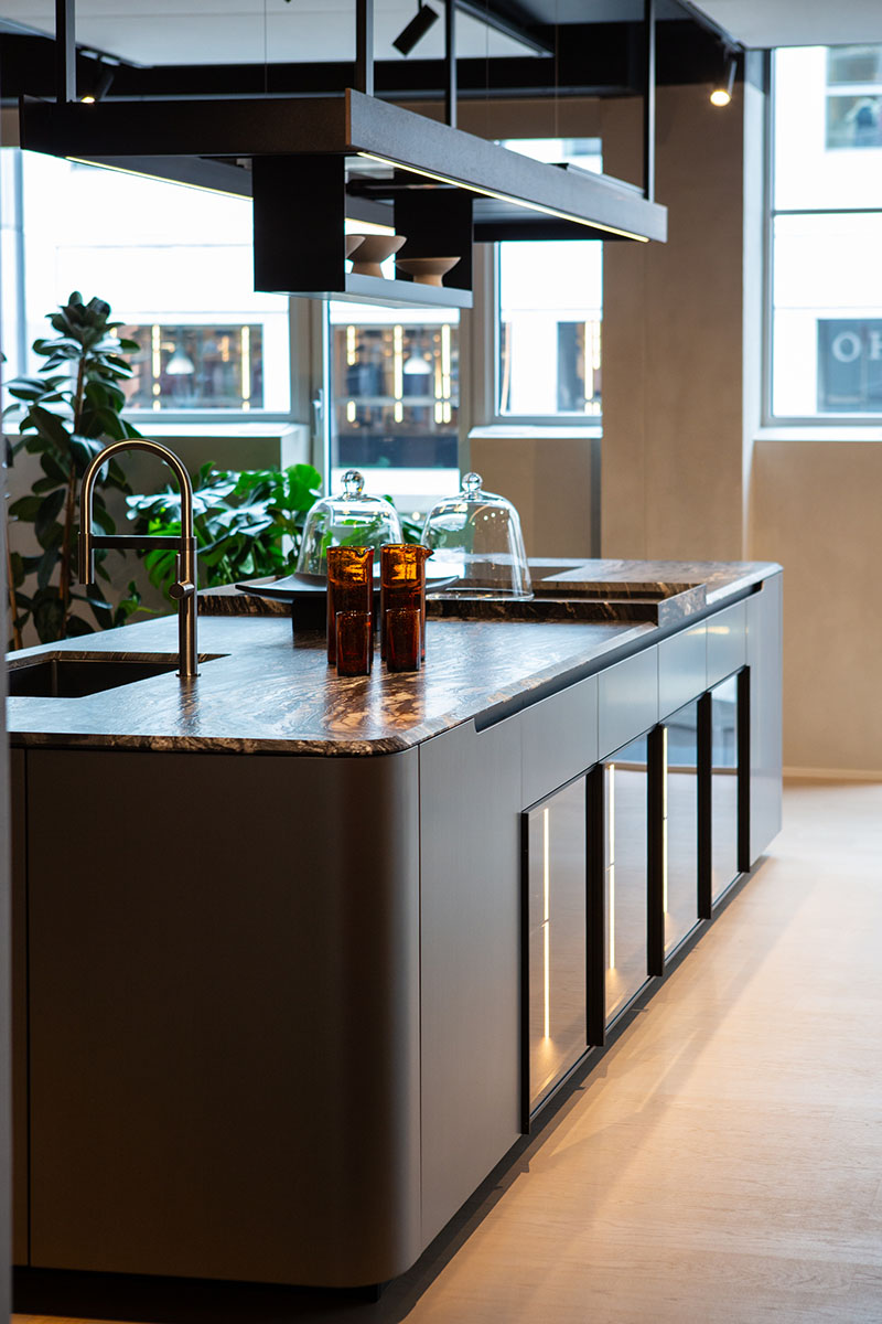 Perspectiva lateral de la cocina metálica con formas curvas de Arrital, con fregadero integrado y vitrina inferior