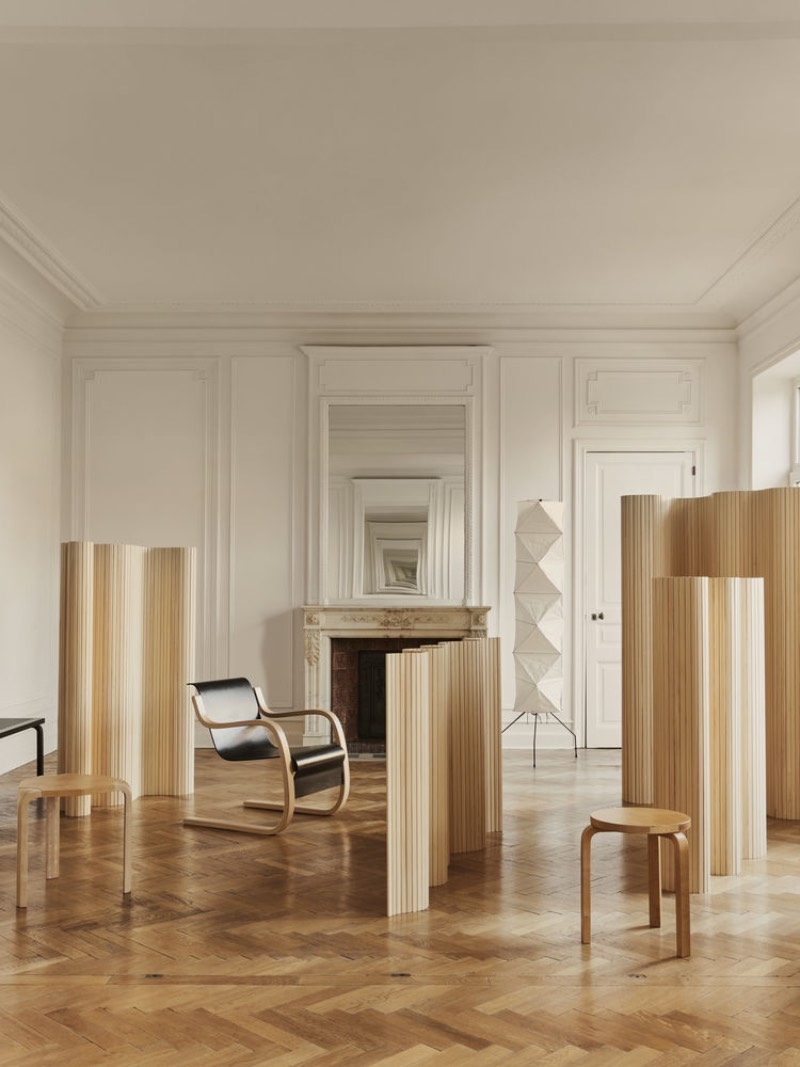 Artek: un salón amplio y luminoso en tonos crudos y tierra, con chimenea, parqué de madera, cuatro biombos, dos banquetas y una silla.