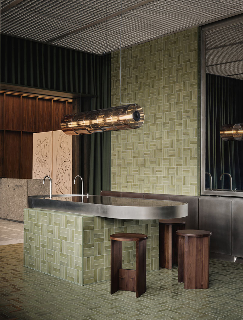 AtelierCarle Oakv: cafetería con barra revestida en cerámica verde y lámpara tubular suspendida