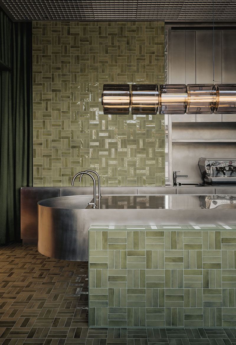 AtelierCarle Oakv: cafetería con barra revestida en cerámica verde y lámpara tubular suspendida