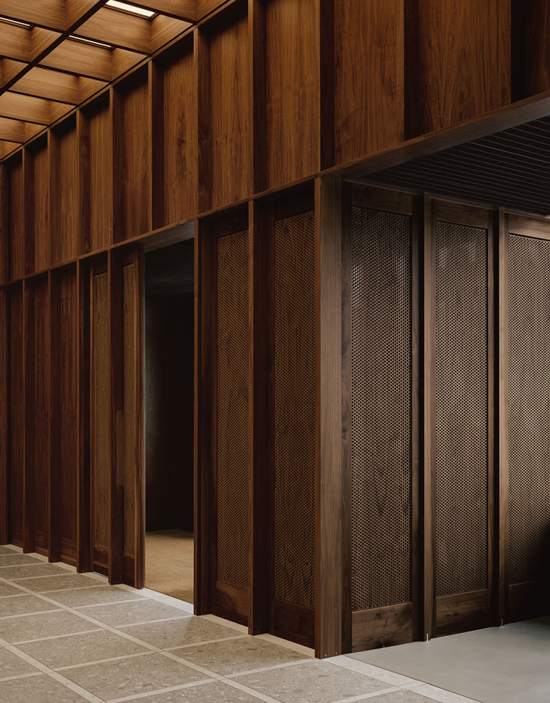 AtelierCarle Oakv: pasillo con paneles perforados de nogal y piso de piedra en retícula