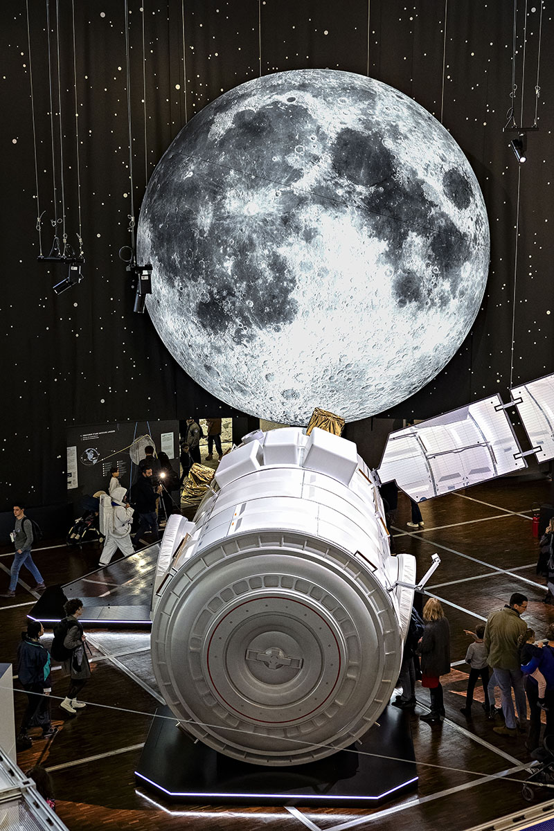Escenografía de la exposición Space Mission en la Cité des Sciences et de l’Industrie con una reproducción a gran escala del módulo I-Hab frente a una Luna iluminada