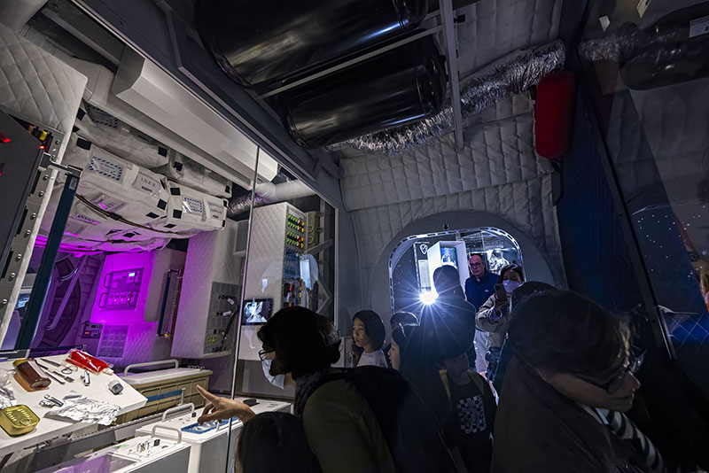 Interior del módulo I-Hab en la exposición Space Mission de la Cité des Sciences et de l’Industrie, con visitantes observando los sistemas de vida y control