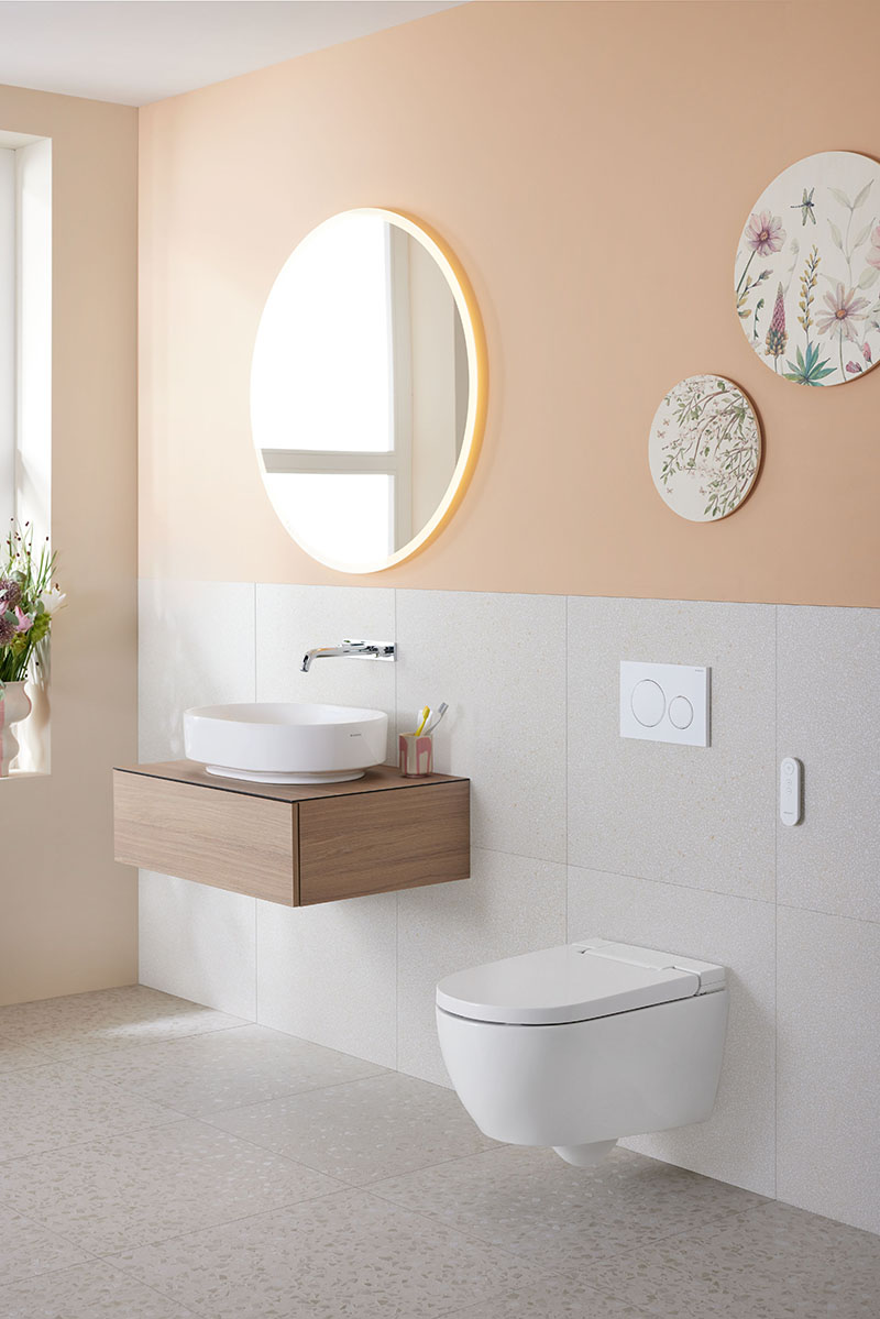 Inodoro bidé Geberit AquaClean: un baño amplio y luminoso en tonos que sobre la pared del espejo tiene un lavabo debajo y un Inodoro bidé Geberit AquaClean suspendido al lado.