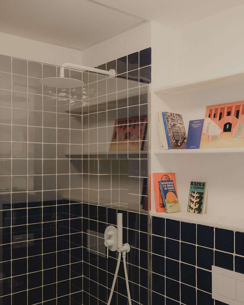 Baño del dúplex en Alboraia de Maria Aucejo, arquitecta, con azulejo azul oscuro y estantería integrada
