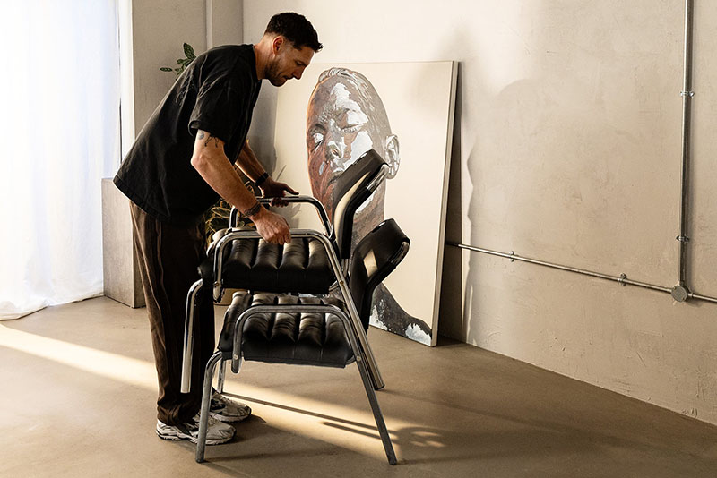 Dos sillas Lounge Chair de Minale en cuero negro apiladas por un hombre en un interior