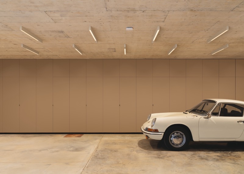 Offset: espacio grande en tonos beige iluminado con lámparas de techo blancas y alargadas de la colección Offset, para alumbrar el espacio, con un coche blanco antiguo en la zona derecha.