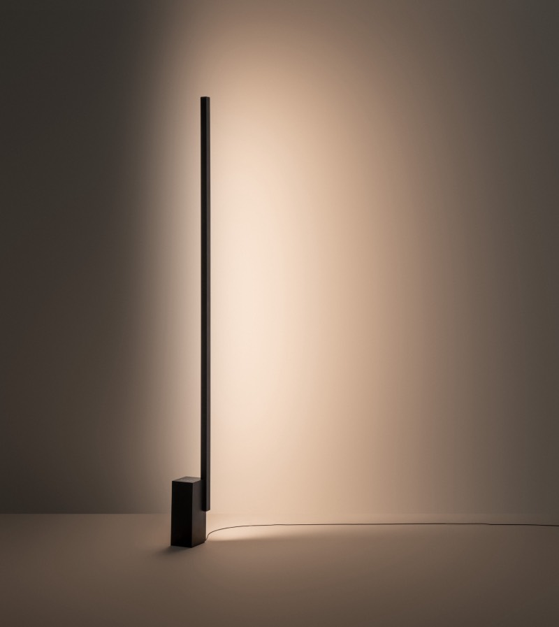 Offset: lámpara de pie negra de la colección Offset que ilumina un espacio diáfano de forma indirecta con la proyección de la luz en la pared.