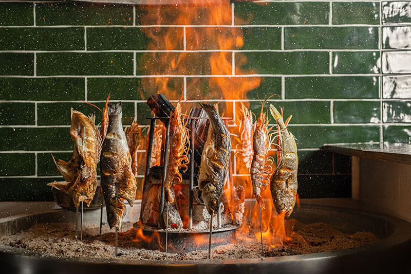 Parrilla del restaurante Toritama Yakitori con mariscos y pescados asándose al fuego