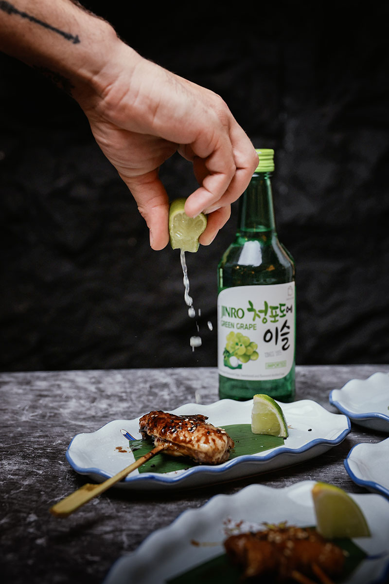 Brocheta del restaurante Toritama Yakitori aderezada con lima y botella de soju en segundo plano