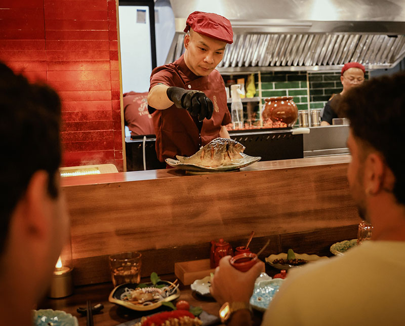 Cocinero del restaurante Toritama Yakitori sirviendo un plato a los comensales en la barra
