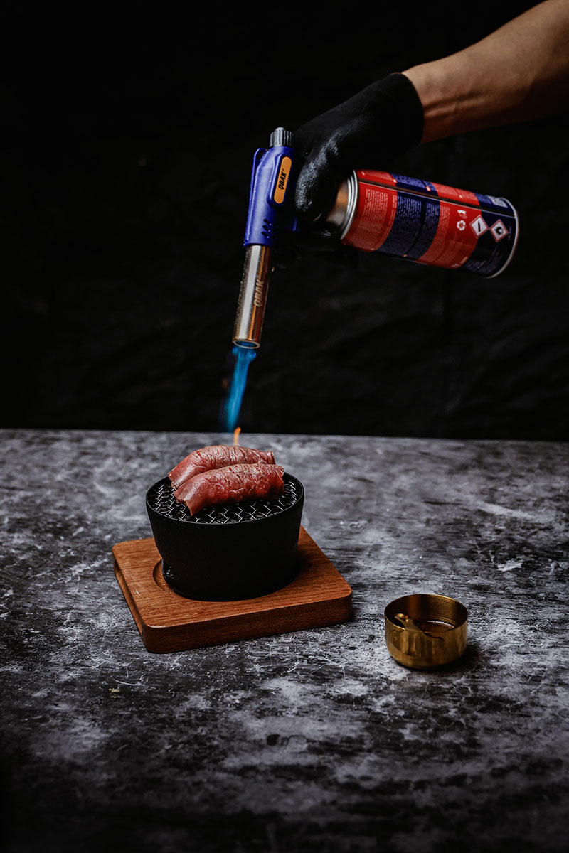 Preparación en el restaurante Toritama Yakitori con carne marcada al soplete sobre mini parrilla