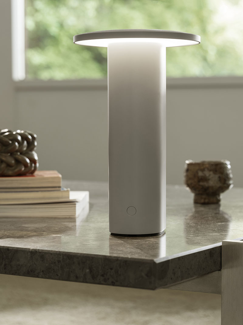 La Solae Lamp de Cecilie Manz para Fritz Hansen está situada sobre una mesa de piedra acompañada de libros y objetos decorativos