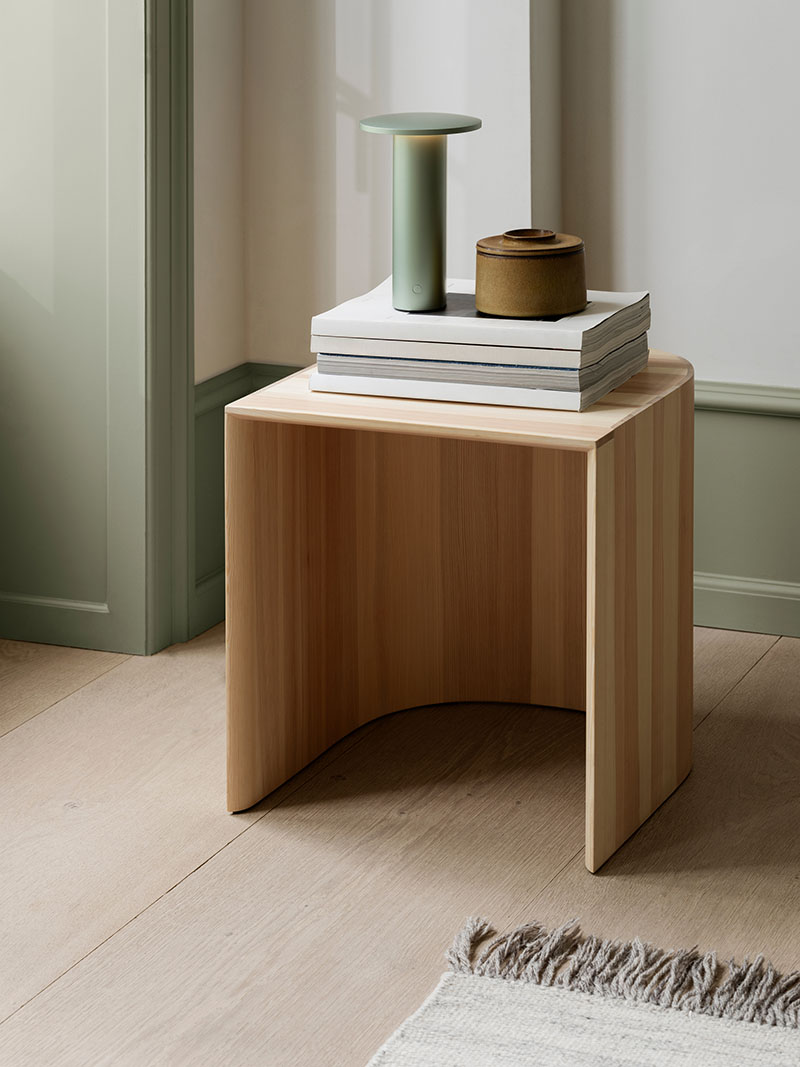 La Solae Lamp de Cecilie Manz para Fritz Hansen se presenta en acabado verde sobre una mesa auxiliar de madera junto a un objeto cerámico