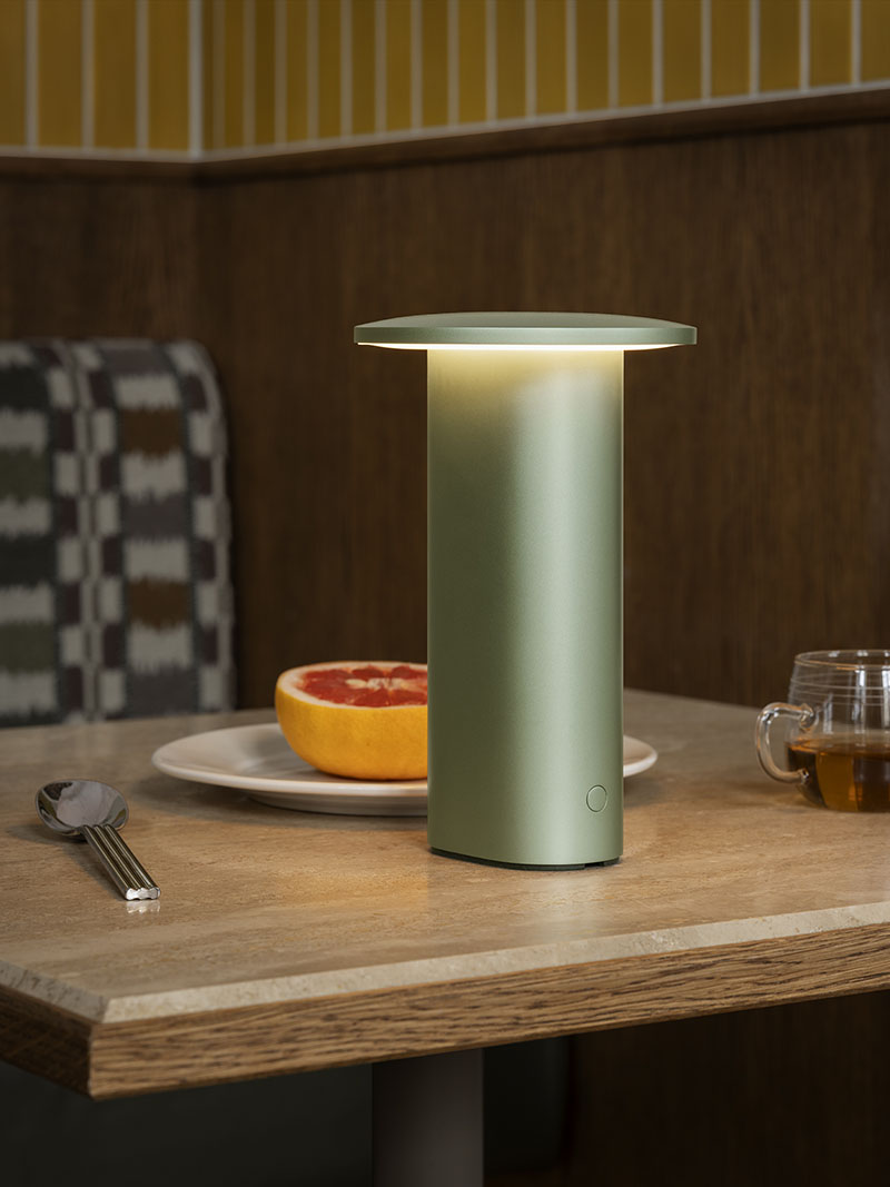 La Solae Lamp de Cecilie Manz para Fritz Hansen se ubica sobre una mesa con un plato de fruta y una taza de té