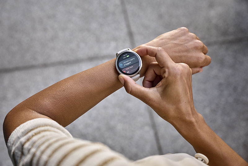 Venu 4: brazos de una mujer desde arriba con un reloj inteligente Garmin Venu 4 con correa blanca en la muñeca izquierda y ajustando las opciones de ejercicio en la pantalla con la mano derecha.