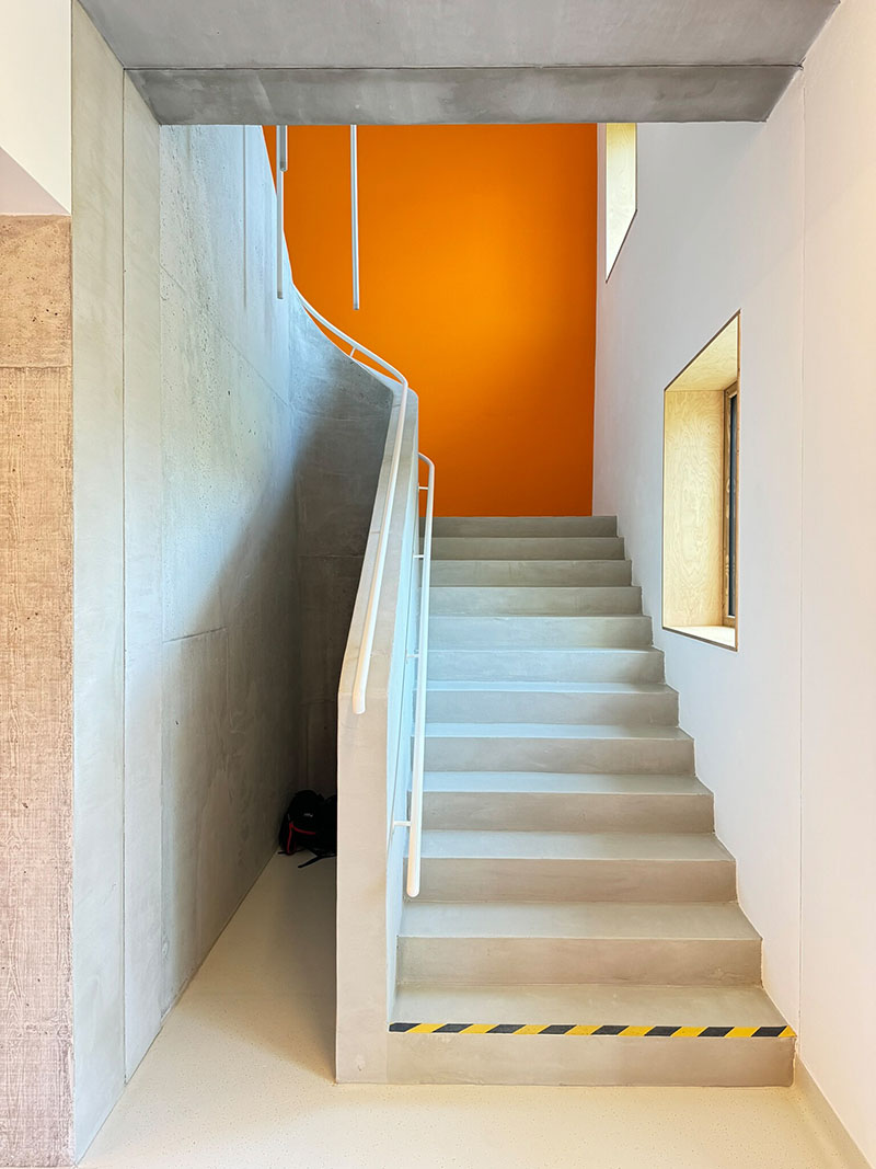 Xtopix Architekti incorpora una escalera de hormigón con barandilla blanca y muro naranja