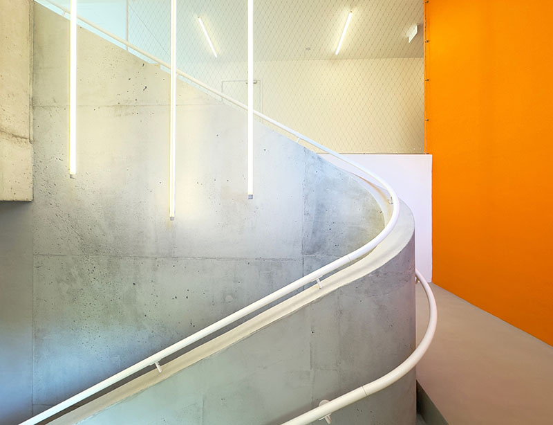 Xtopix Architekti resalta el encuentro entre la escalera curva de hormigón y la pared en color naranja