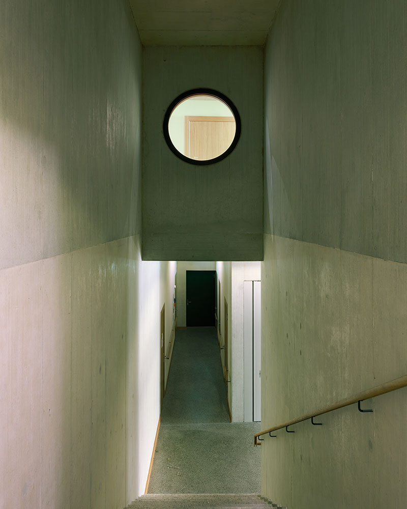 pasillo interior del edificio residencial de Borna-Park diseñado por Malte Kloes Architekten, con ventanal circular que permite la entrada de luz natural