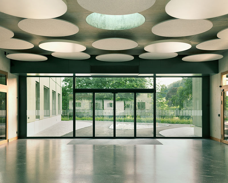 Borna-Park, Malte Kloes Architekten: área de entrada del edificio residencial con plafones acústicos circulares en el techo