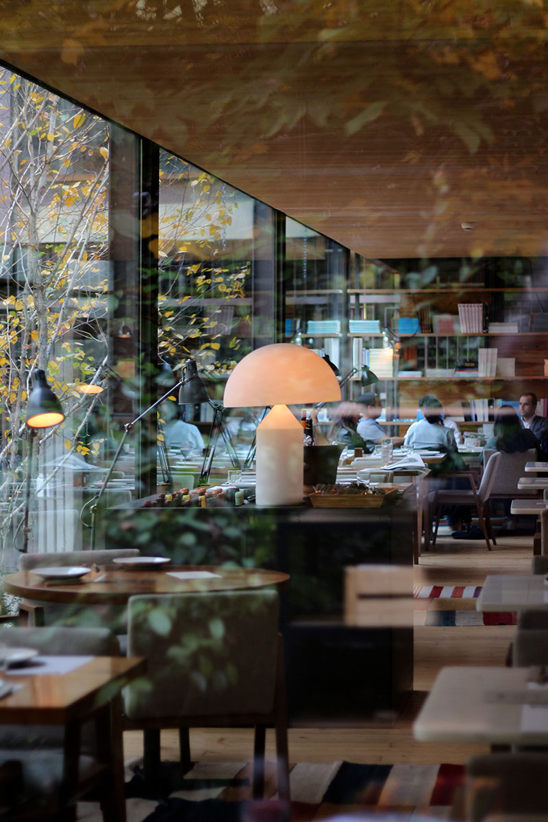 El interior del restaurante Bosco de Lobos refleja el otoño en los ventanales, con luces cálidas y árboles desnudos al fondo