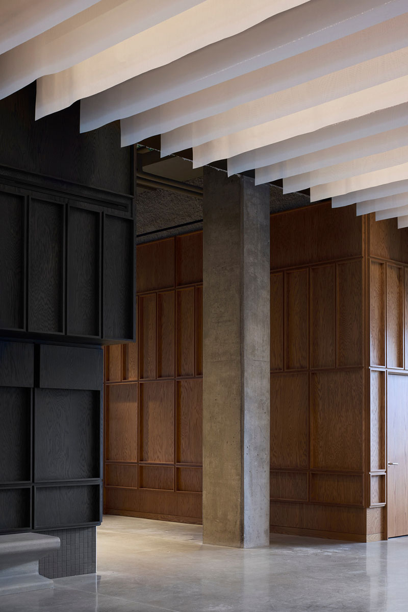 Un pasillo del Centre Sanaaq presenta paneles de madera y superficies negras junto a un pilar de hormigón