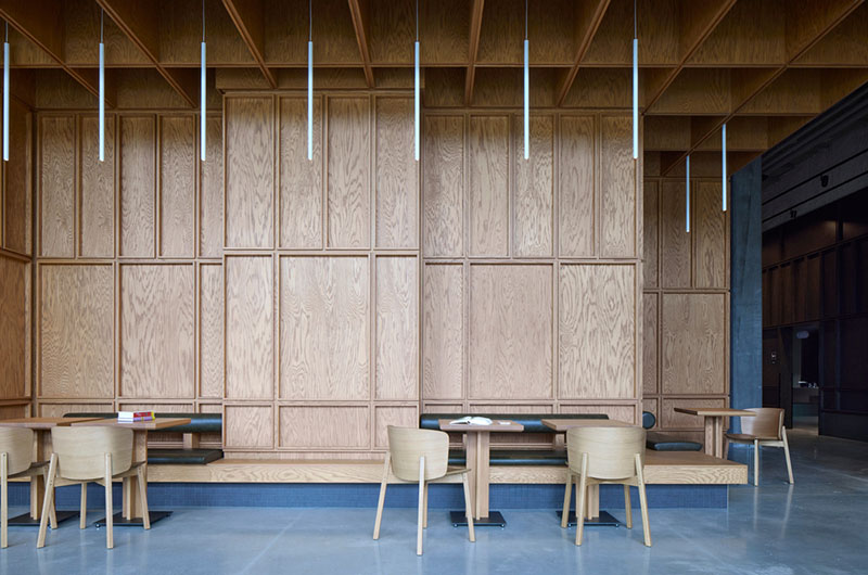 Un área de lectura del Centre Sanaaq reúne mesas, sillas y paneles de madera de gran formato