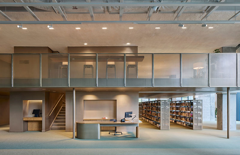 La zona de atención de la biblioteca del Centre Sanaaq muestra un mostrador central, estantes y una mezzanine
