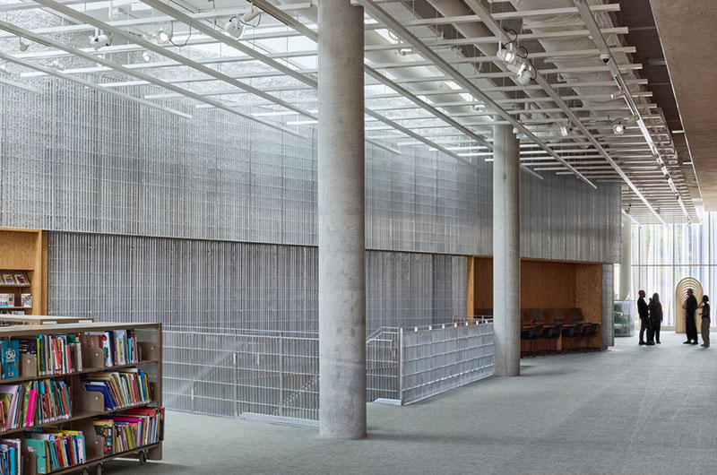 La planta superior de la biblioteca del Centre Sanaaq reúne estanterías, pilares de hormigón y cerramientos metálicos