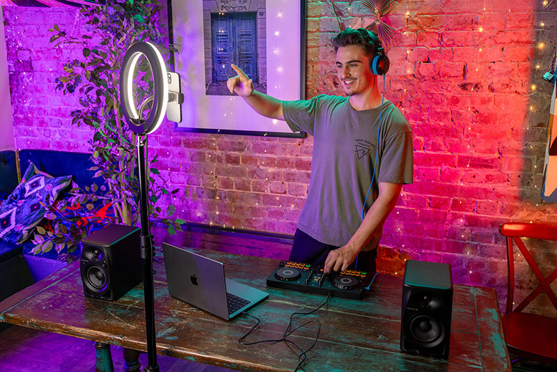 Usuario utilizando la controladora DJ de AlphaTheta con portátil, altavoces y luz de grabación