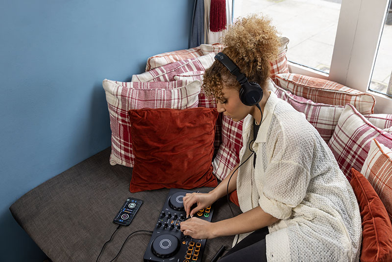 Usuaria usando la controladora DJ de AlphaTheta conectada a un móvil mientras se sienta en un sofá