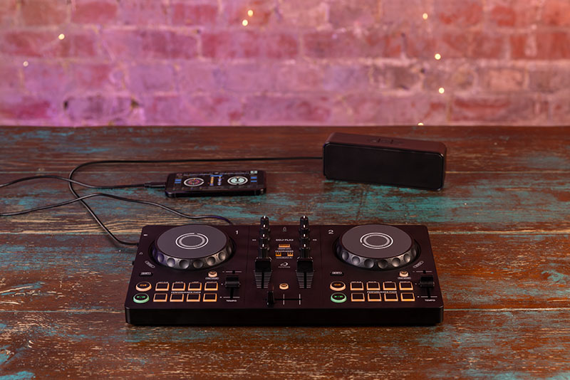 Controladora DJ de AlphaTheta conectada a un smartphone y un altavoz portátil sobre una mesa