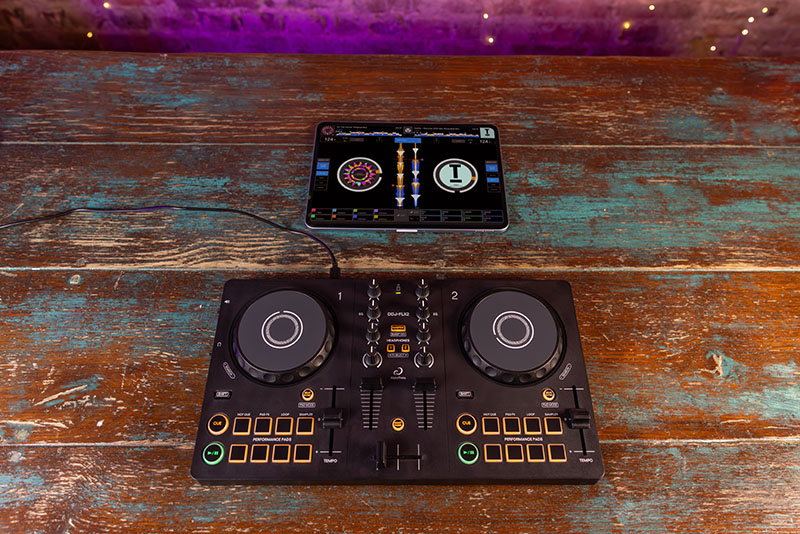 Controladora DJ de AlphaTheta conectada a una tablet con software de mezcla visible en pantalla