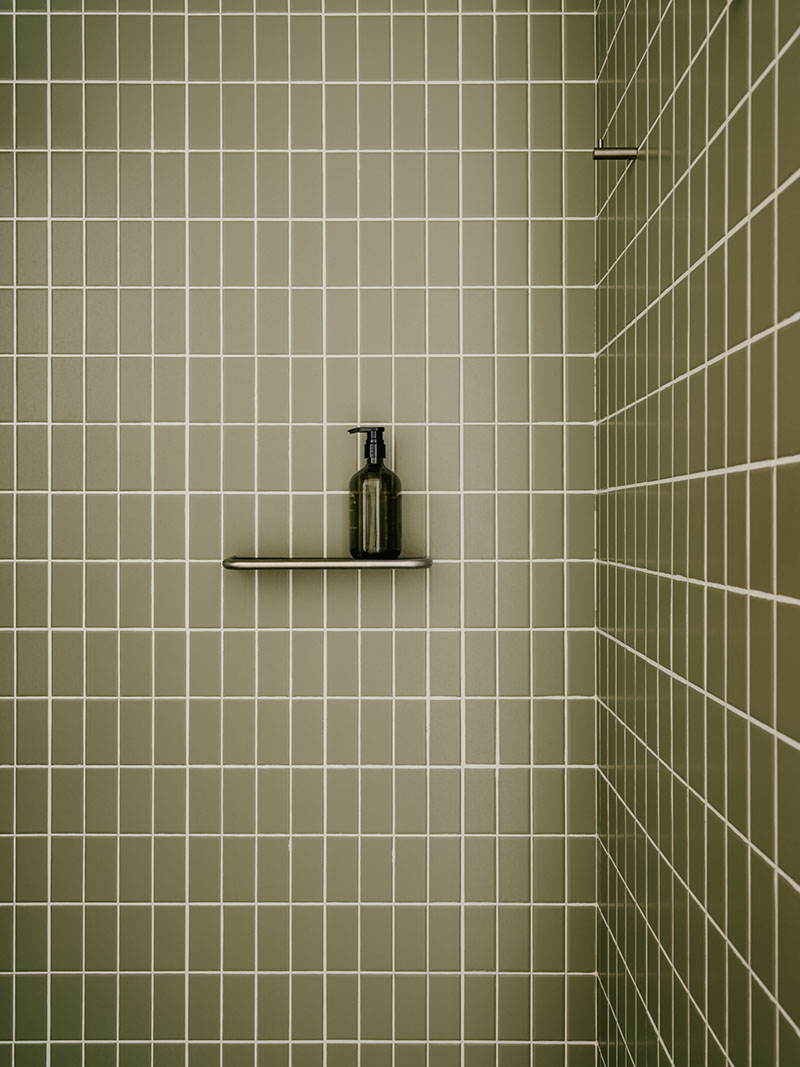 Iriondo Studio detalla la ducha con azulejo cerámico verde y repisa metálica para accesorios.
