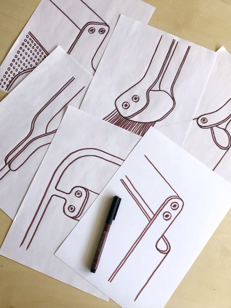 Eldvarm Fumi: bocetos de varias piezas de Eldvarm de la colección Fumi para leña dibujados en folios blancos sobre una mesa de madera.