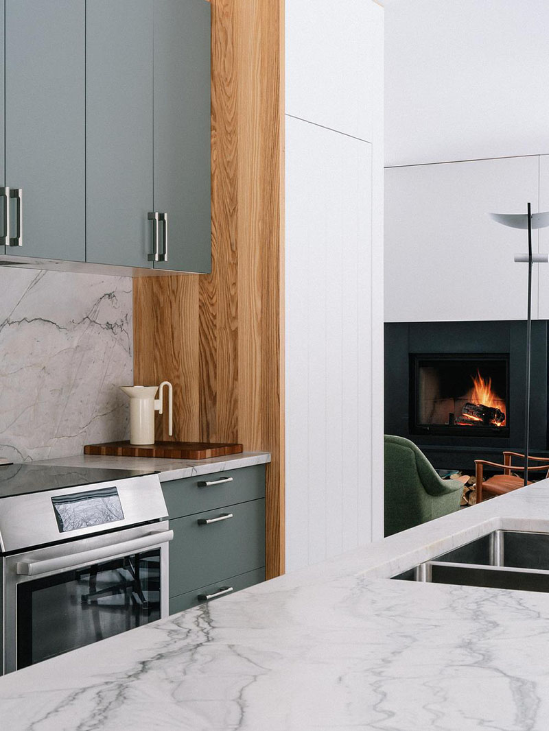 EM architecture detalla el acabado de la cocina con mármol, madera y vista hacia la chimenea
