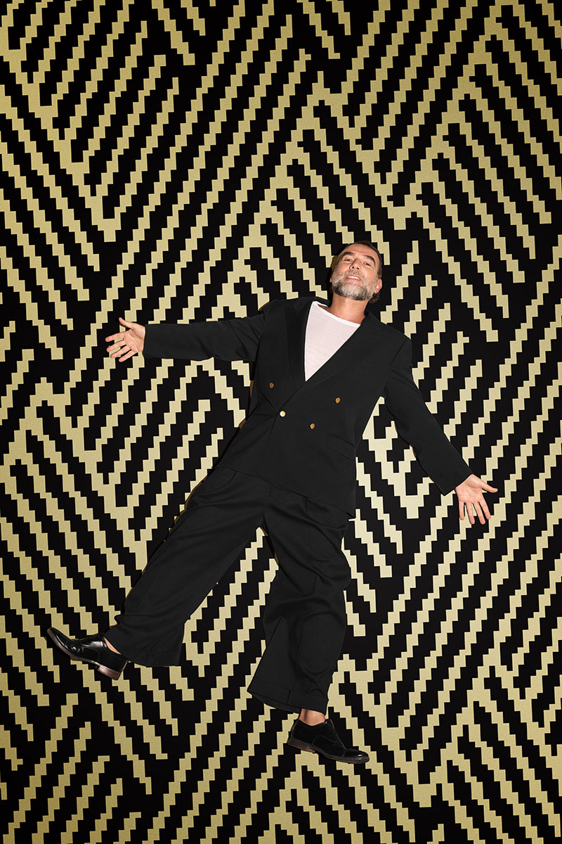 Stefano Seletti posa tumbado sobre un fondo con el diseño de Iqos Iluma i x Seletti