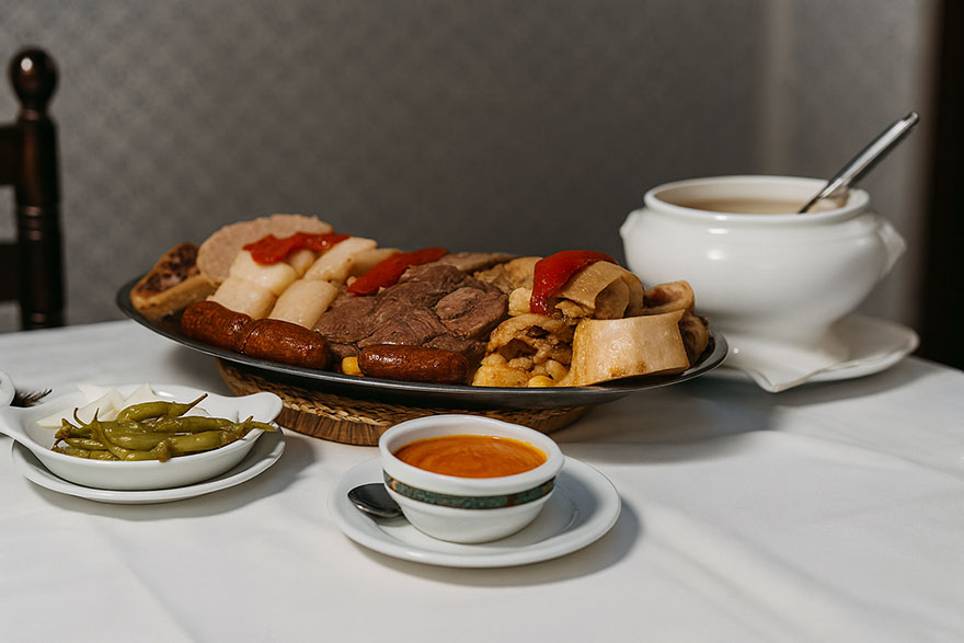 El cocido madrileño de La Gran Tasca servido en mesa junto a su sopa, salsa y guarniciones