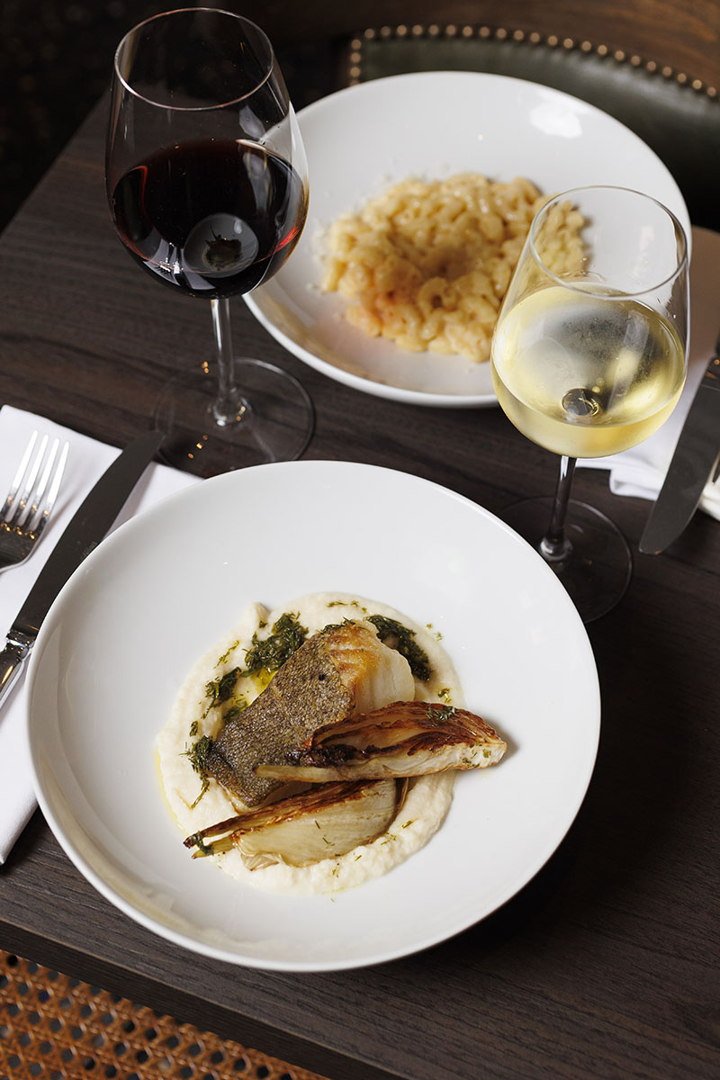 Un plato de pescado y dos copas de vino se presentan sobre una mesa del restaurante L'Arrêt en París