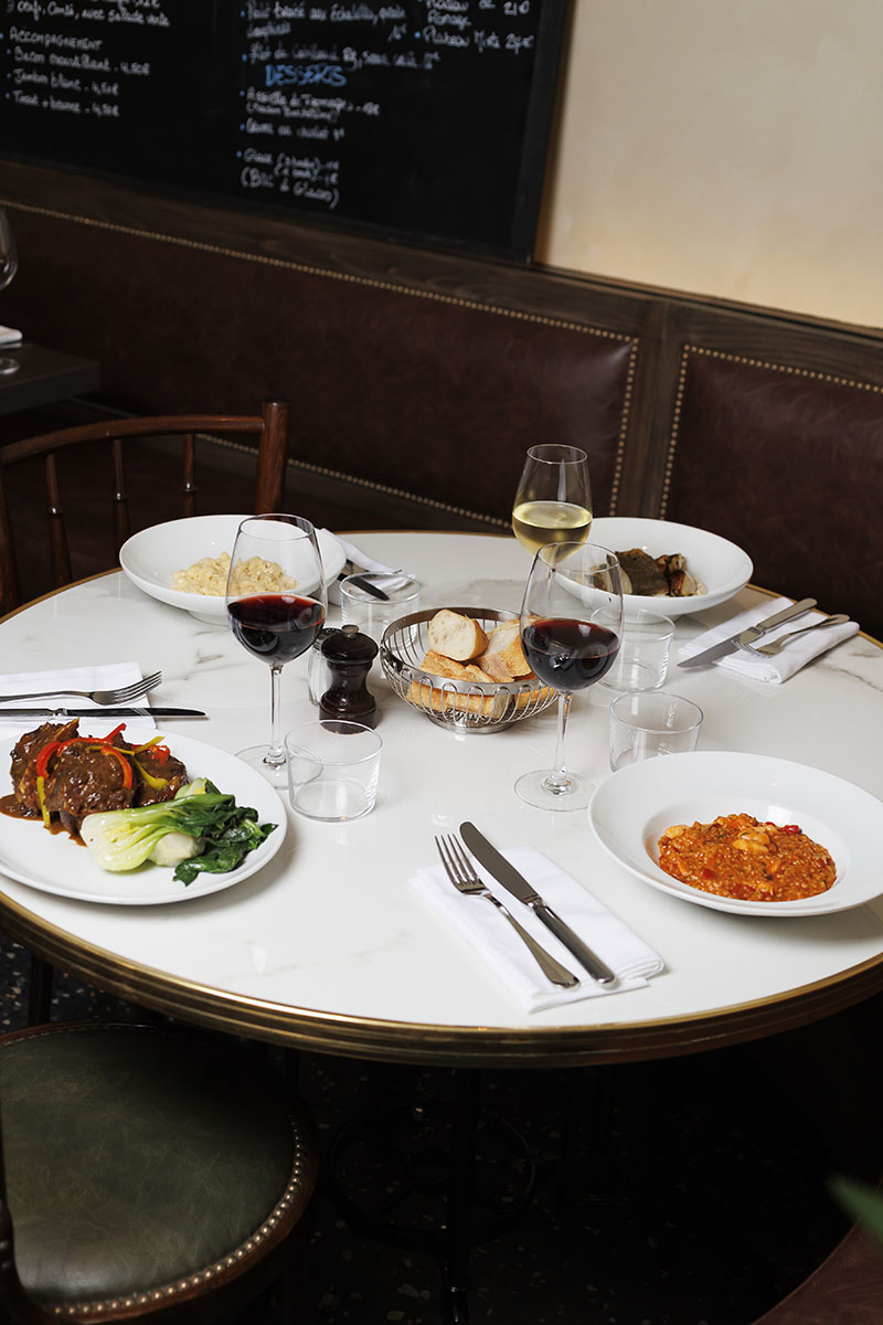 Una mesa redonda del restaurante L'Arrêt en París reúne varios platos, pan y copas de vino