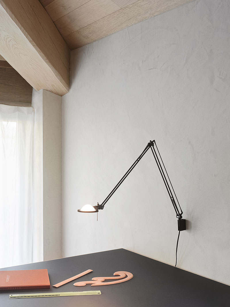 Luceplan: lámpara de pared de Luceplan en negro sobre una mesa negra que contiene tres tipos de reglas diferentes y un cuaderno.