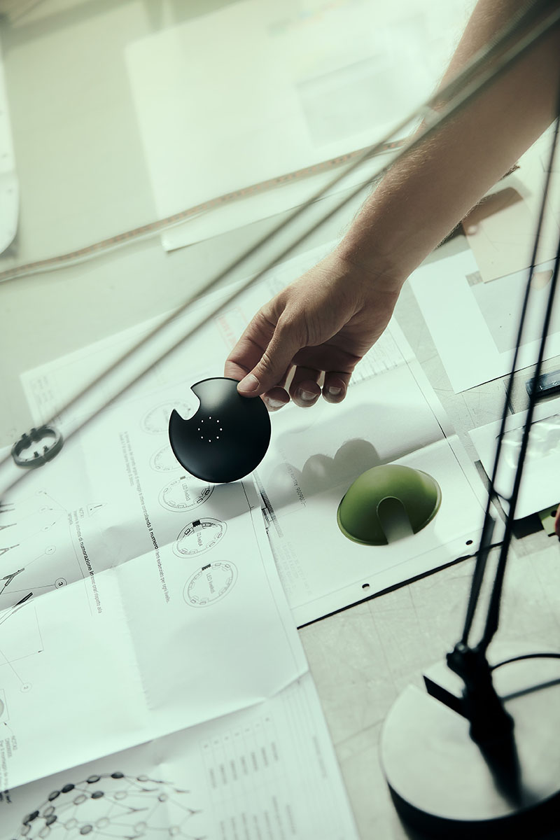 Luceplan: foto del brazo de una persona con una de las piezas de una lámpara de mesa que está montando mirando las instrucciones que tiene debajo y junto a la base de la lámpara ya lista.